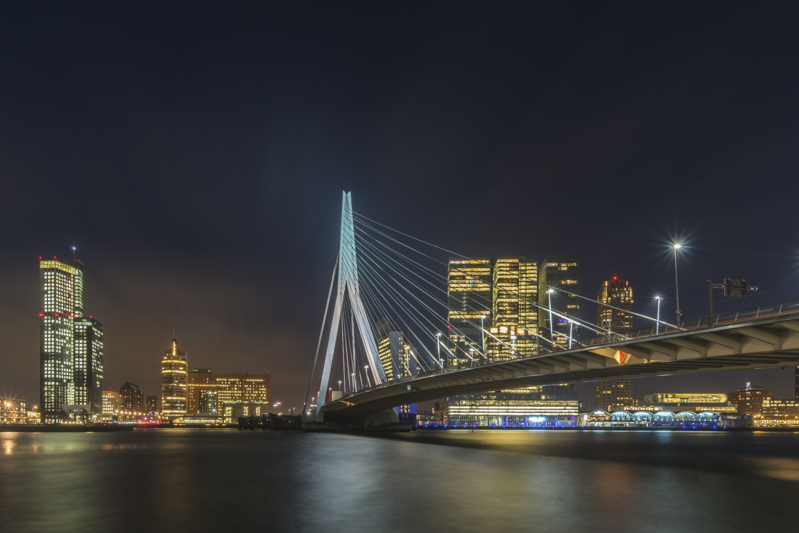 Als de nacht over Rotterdam (zuid-Holland, Nederland) valt, ontwaken de lichten. Een schitterend gezicht om deze wisselwerking mee te maken. De stad werd mooi verlicht en de Erasmusbrug lag er mooi bij! Een fijne plek voor cityscape fotografie, landschapsfotografie en nachtfotografie te beoefenen.
