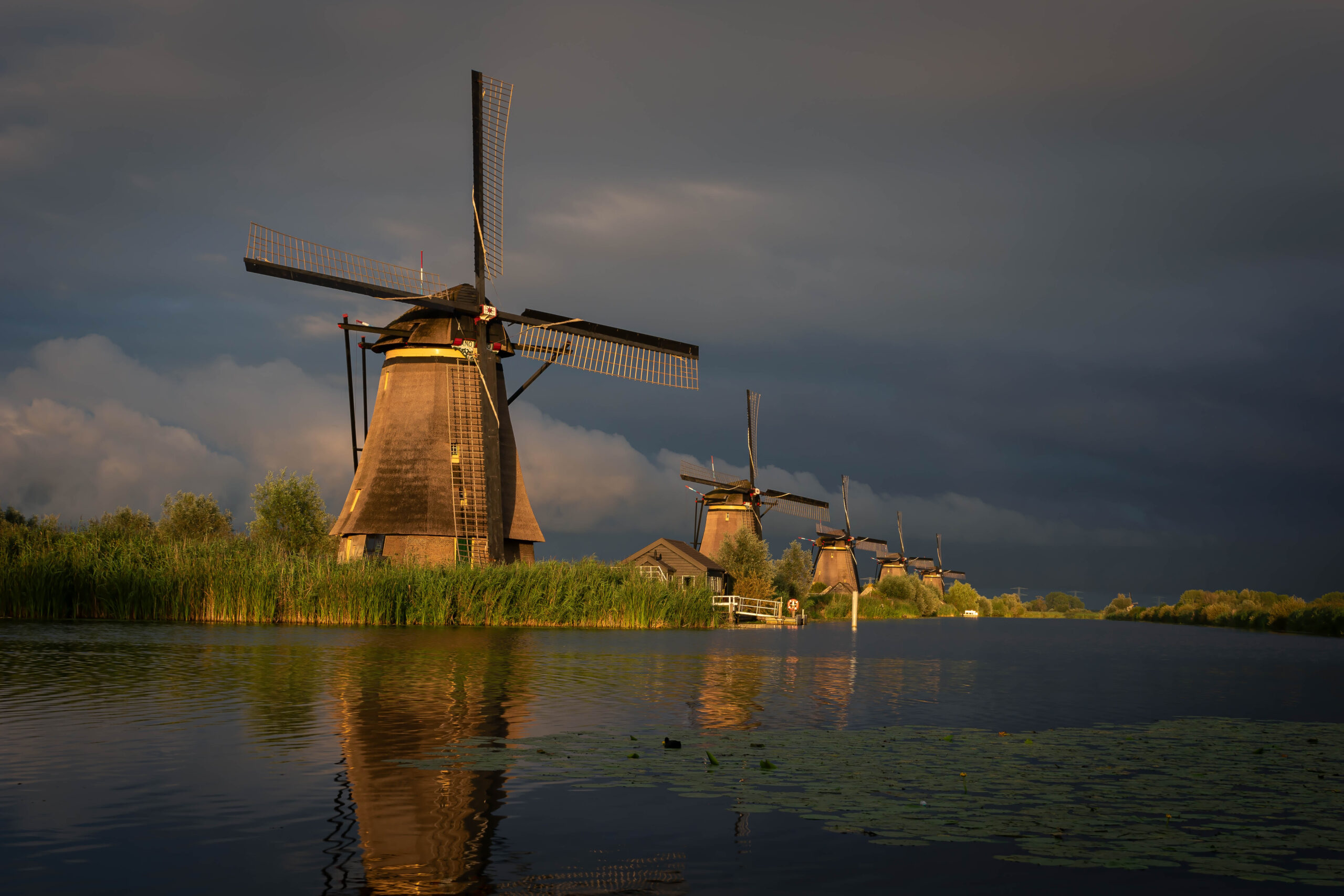 Deze foto is gemaakt bij werelderfgoed Kinderdijk (Zuid-Holland, Nederland). Heel de dag was het bewolkt en had het geregend, maar 's avonds trok de lucht mooi open. Dit leverde een fantastisch gouden uur (golden hour) op. Zeker in combinantie met de dreigende regenwolken op de achtergrond.