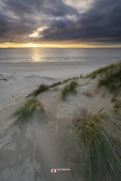 Deze foto is gemaakt aan het strand van Rockanje (Zuid-Holland, Nederland). Heel de dag was het grijs weer, maar 's middags vertoonde het wolkendek opeens gaten. En daarom maar naar deze plek gereden. Een schitterende zonsondergang was het resultaat.