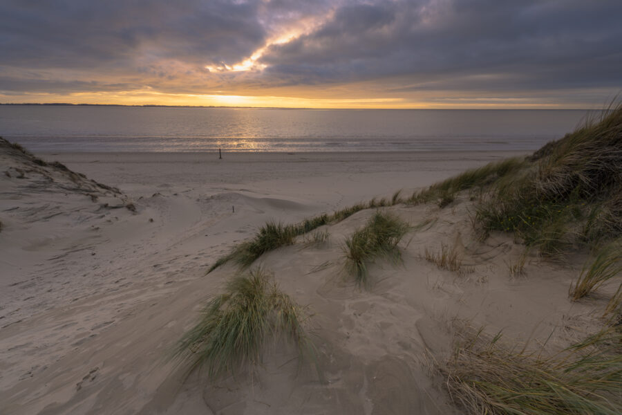 Deze foto is gemaakt aan het strand van Rockanje (Zuid-Holland, Nederland). Heel de dag was het grijs weer, maar 's middags vertoonde het wolkendek opeens gaten. En daarom maar naar deze plek gereden. Een schitterende zonsondergang, met een enorme gouden gloed viel me ten deel. Genoten aan dit strand!