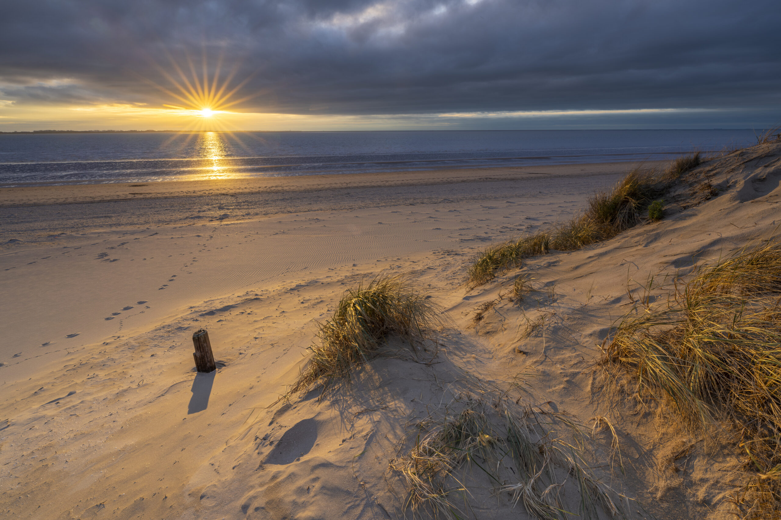 Deze foto is gemaakt aan het strand van Rockanje (Zuid-Holland, Nederland). Heel de dag was het grijs weer, maar 's middags vertoonde het wolkendek opeens gaten. En daarom maar naar deze plek gereden. Een schitterende zonsondergang, met een enorme gouden gloed viel me ten deel. Genoten aan dit strand!