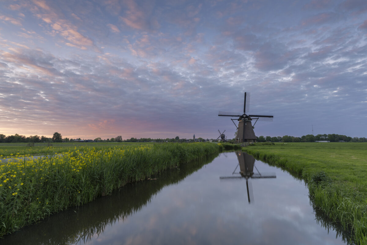 Tijdens de zonsondergang is het goed om ook achterom te krijgen. Dan zie je wat het laatste zonlicht doet in het landschap achter je. Hier kleurde de wolken erg mooi mee. Een foto van de molens langs de Tiendweg bij Streefkerk (Zuid-Holland, Nederland).