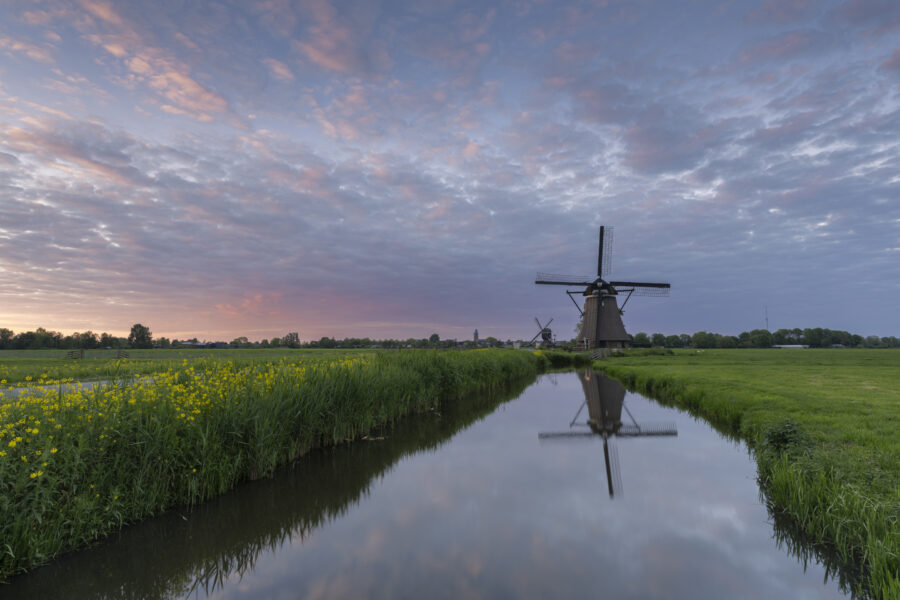 Tijdens de zonsondergang is het goed om ook achterom te krijgen. Dan zie je wat het laatste zonlicht doet in het landschap achter je. Hier kleurde de wolken erg mooi mee. Een foto van de molens langs de Tiendweg bij Streefkerk (Zuid-Holland, Nederland).