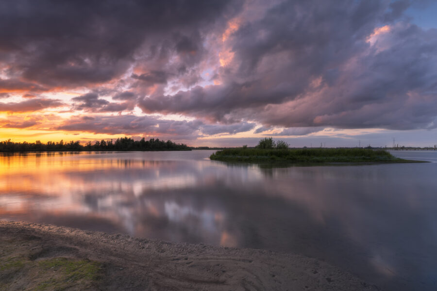 Een schitterende zonsondergang boven Nationaal Park De Biesbosch. Achter mij dreigde alweer een volgende onweersbui, maar voor mij ging de zon schitterend onder. Het zette de dreigende wolken in brand. Door het vele vocht in de lucht waren de kleuren nog intenser. Heerlijk om deze kleuren weerspiegelt te zien in het water. Een heerlijk moment om deze landschapsfoto te kunnen maken.