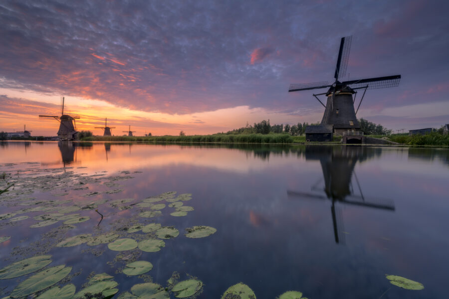 Een schitterende zonsondergang boven de molens van UNESCO Werelderfgoed de Kinderdijkse Molens te Kinderdijk (Zuid-Holland, Nederland). Deze dag werd een hitterecord bereik en was de lucht strakblauw. Maar 's avonds werd bewolking opgegeven. Ik ben naar dit bekende plekje gereden om heerlijk te genieten van de omstandigheden het het fotograferen van dit landschap.