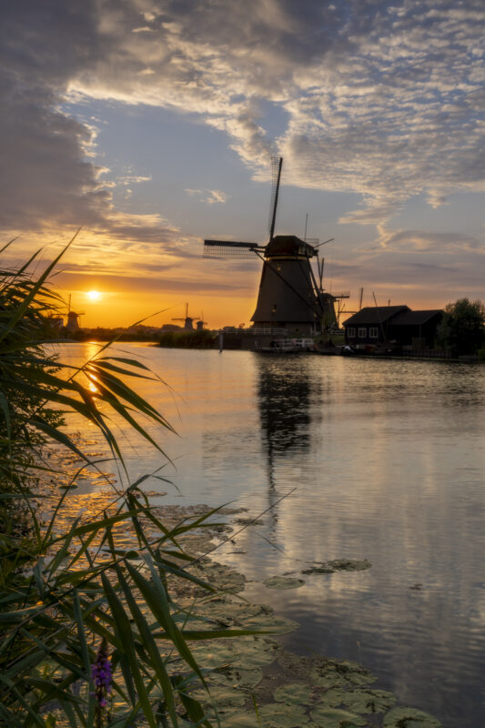 Een schitterende zonsondergang boven de molens van UNESCO Werelderfgoed de Kinderdijkse Molens te Kinderdijk (Zuid-Holland, Nederland). Deze dag werd een hitterecord bereik en was de lucht strakblauw. Maar 's avonds werd bewolking opgegeven. Ik ben naar dit bekende plekje gereden om heerlijk te genieten van de omstandigheden het het fotograferen van dit landschap.