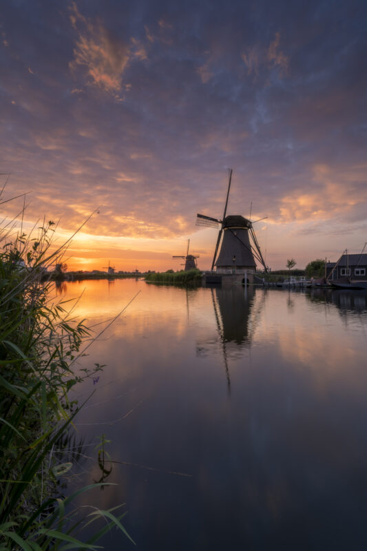 Een schitterende zonsondergang boven de molens van UNESCO Werelderfgoed de Kinderdijkse Molens te Kinderdijk (Zuid-Holland, Nederland). Deze dag werd een hitterecord bereik en was de lucht strakblauw. Maar 's avonds werd bewolking opgegeven. Ik ben naar dit bekende plekje gereden om heerlijk te genieten van de omstandigheden het het fotograferen van dit landschap.