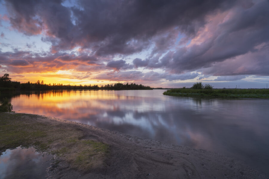 Een schitterende zonsondergang boven Nationaal Park De Biesbosch. Achter mij dreigde alweer een volgende onweersbui, maar voor mij ging de zon schitterend onder. Het zette de dreigende wolken in brand. Door het vele vocht in de lucht waren de kleuren nog intenser. Heerlijk om deze kleuren weerspiegelt te zien in het water. Een heerlijk moment om deze landschapsfoto te kunnen maken.