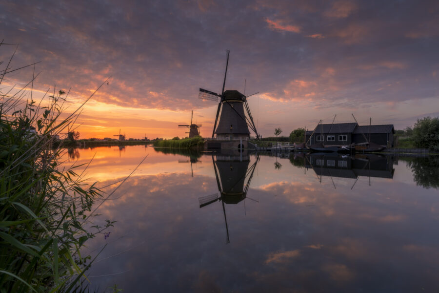 Een schitterende zonsondergang boven de molens van UNESCO Werelderfgoed de Kinderdijkse Molens te Kinderdijk (Zuid-Holland, Nederland). Deze dag werd een hitterecord bereik en was de lucht strakblauw. Maar 's avonds werd bewolking opgegeven. Ik ben naar dit bekende plekje gereden om heerlijk te genieten van de omstandigheden het het fotograferen van dit landschap.