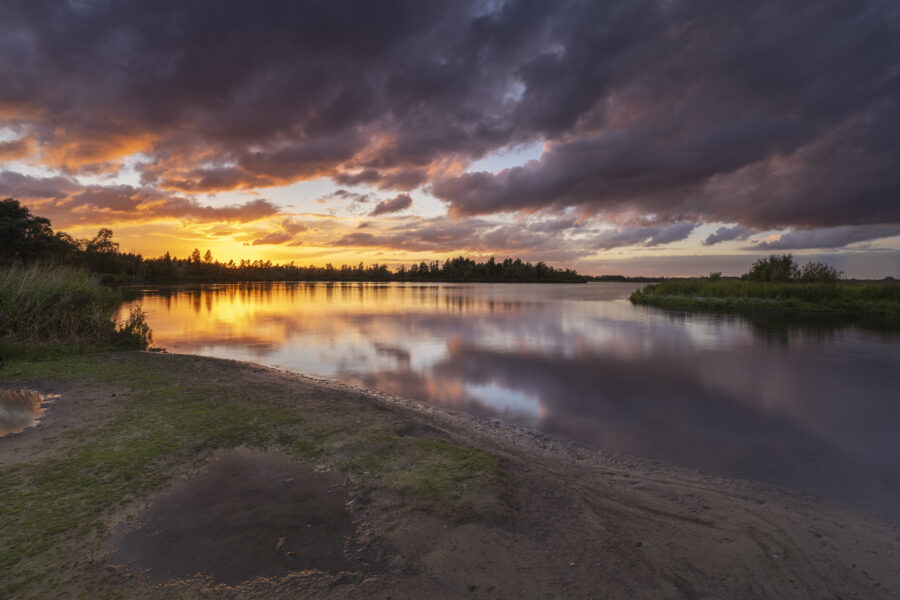 Een schitterende zonsondergang boven Nationaal Park De Biesbosch. Achter mij dreigde alweer een volgende onweersbui, maar voor mij ging de zon schitterend onder. Het zette de dreigende wolken in brand. Door het vele vocht in de lucht waren de kleuren nog intenser. Heerlijk om deze kleuren weerspiegelt te zien in het water. Een heerlijk moment om deze landschapsfoto te kunnen maken.