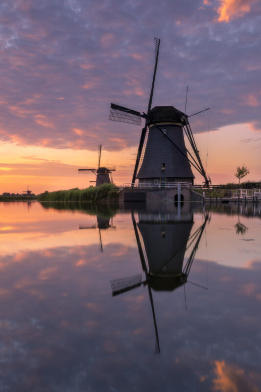 Een schitterende zonsondergang boven de molens van UNESCO Werelderfgoed de Kinderdijkse Molens te Kinderdijk (Zuid-Holland, Nederland). Deze dag werd een hitterecord bereik en was de lucht strakblauw. Maar 's avonds werd bewolking opgegeven. Ik ben naar dit bekende plekje gereden om heerlijk te genieten van de omstandigheden het het fotograferen van dit landschap.