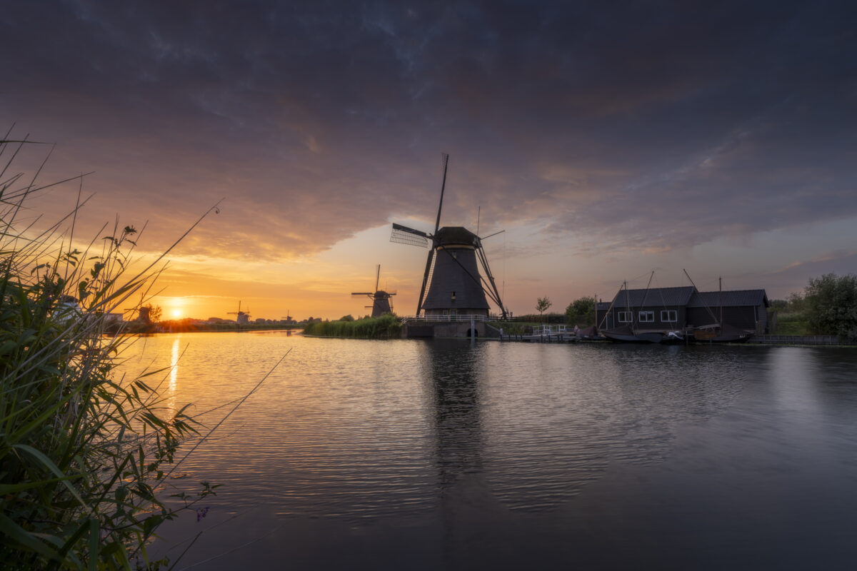 Een schitterende zonsondergang boven de molens van UNESCO Werelderfgoed de Kinderdijkse Molens te Kinderdijk (Zuid-Holland, Nederland). Deze dag werd een hitterecord bereik en was de lucht strakblauw. Maar 's avonds werd bewolking opgegeven. Ik ben naar dit bekende plekje gereden om heerlijk te genieten van de omstandigheden het het fotograferen van dit landschap.